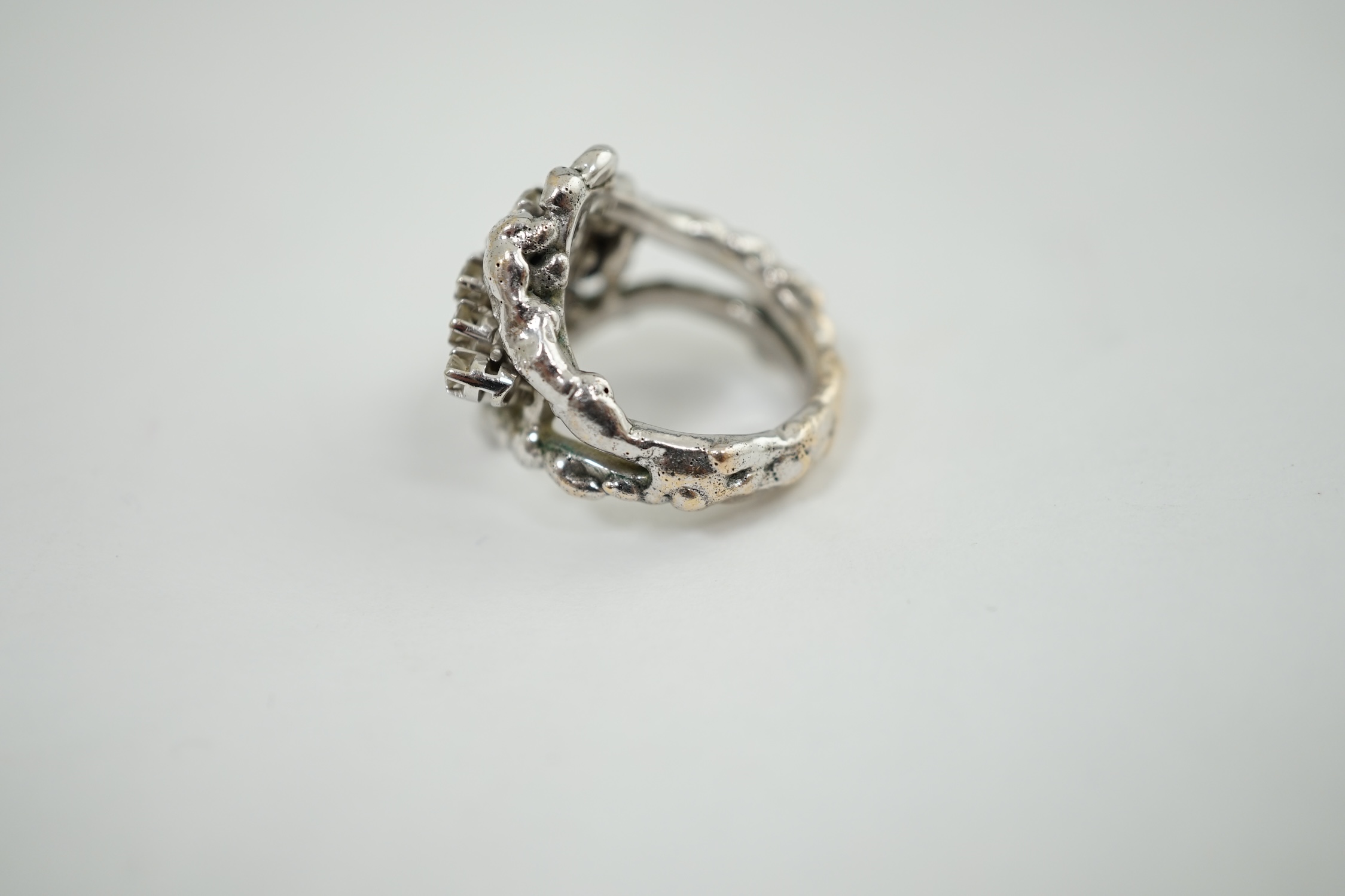 A modernist cast unmarked white metal dress ring, claw set with twenty small diamonds